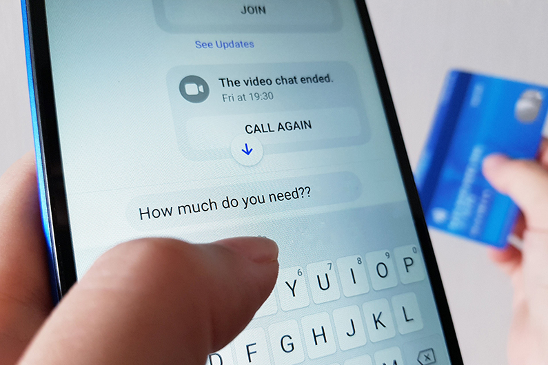 A smartphone showing a scam exchange requesting money with a blue credit card in the background.
