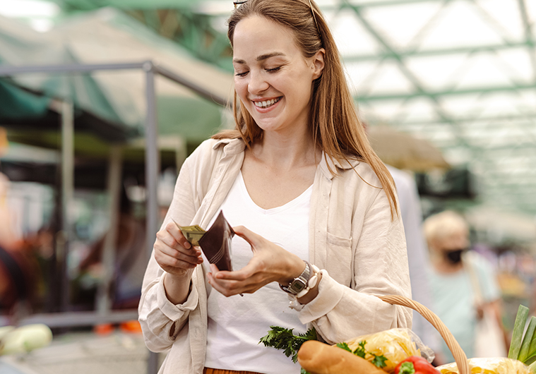 A young woman pulling cash out of her wallet to pay for a basket of food.