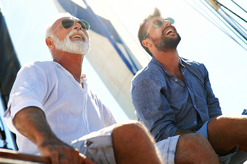 Two individuals sitting on a boat with sails in the background.