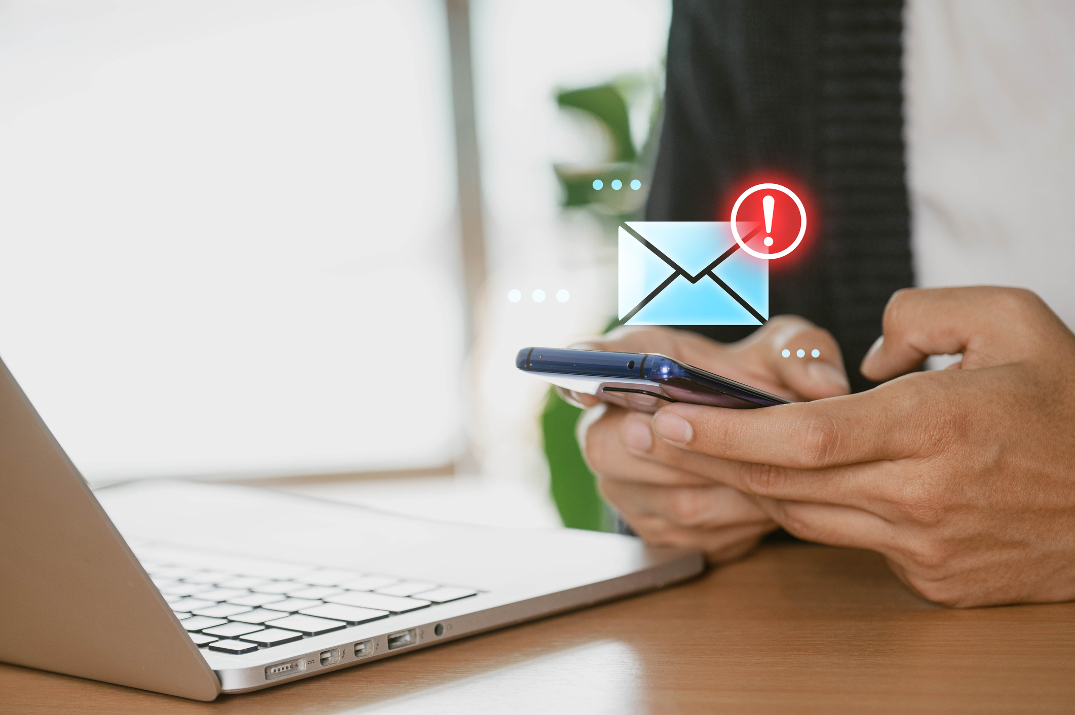 Woman sits at a desk and uses a laptop computer with a phishing warning on the screen.